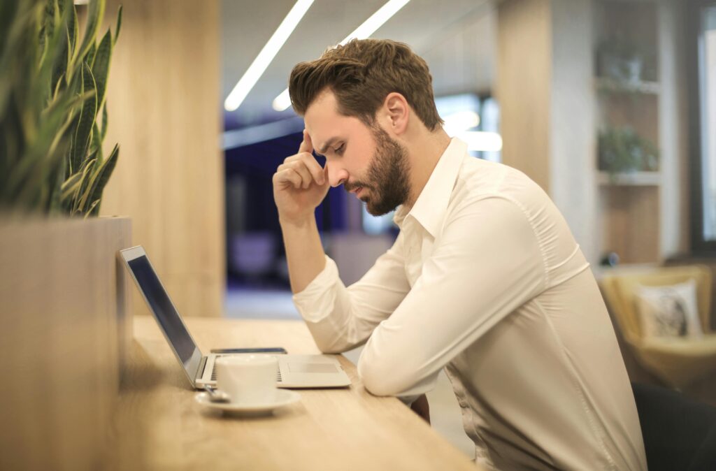 A thoughtful man in a shirt works on his laptop at a modern indoor office space.